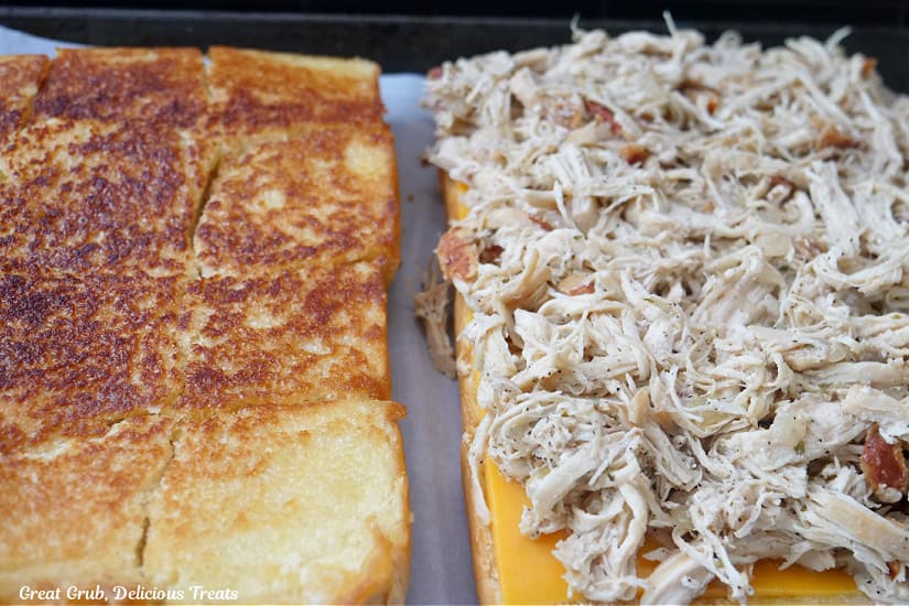 Grilled slider buns with shredded chicken, cheese, and bacon crumbles on one side of the buns.