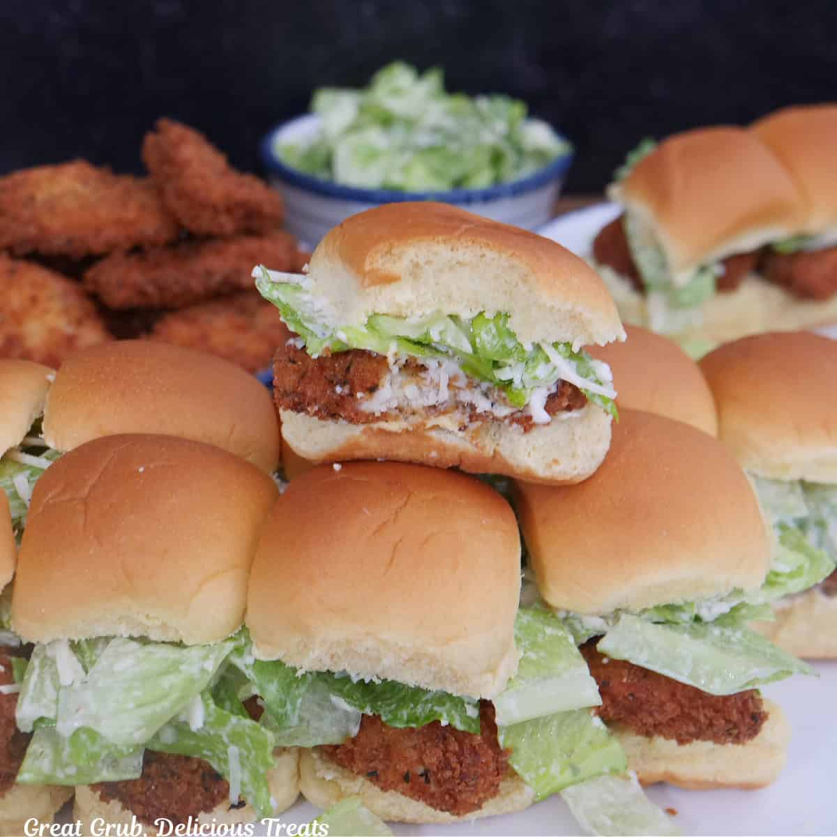 Bite-size chicken Caesar salad sliders on a white surface with a bite taken out of one of the sliders.