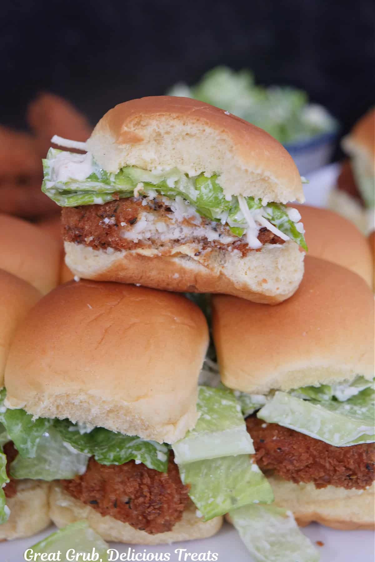 Mini chicken sliders on a white surface with a bite taken out of the slider on top of two other sliders.