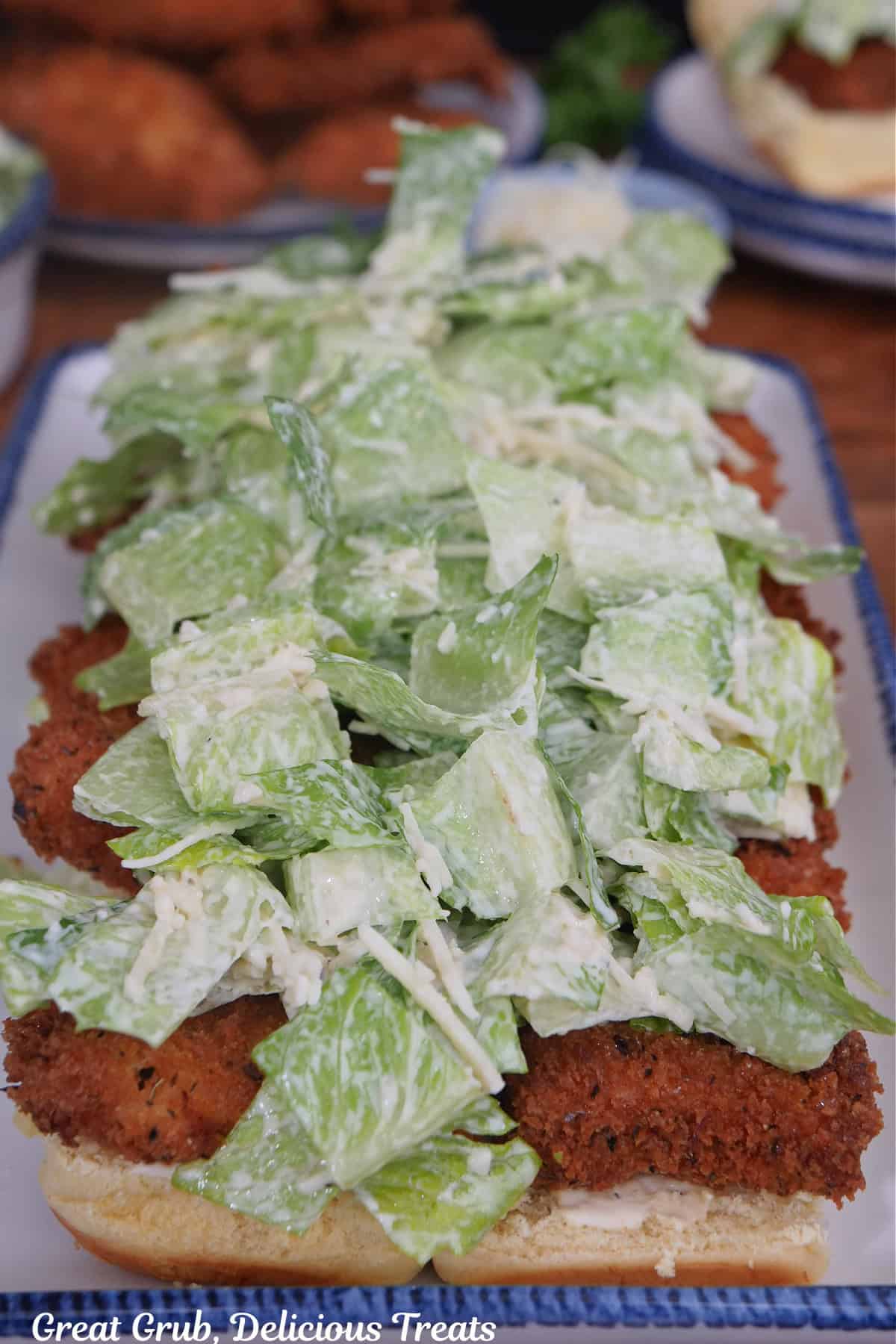 Slider buns with fried chicken and Caesar salad on top of them.