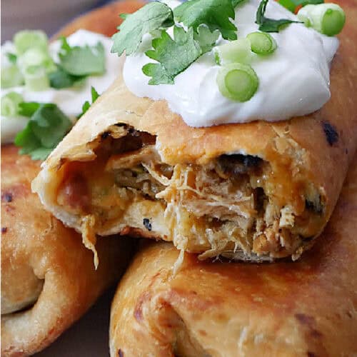 Three fried chicken chimichangas on a plate with sour cream, green onions, and cilantro on top.