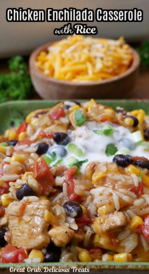 A serving of enchilada casserole with chicken and rice on a green plate with a bowl of shredded cheese in the background.