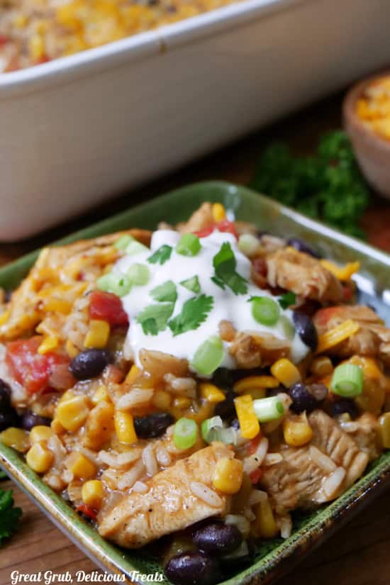 A close up of a serving of sliced chicken pieces, rice, corn, beans, cheese, sour cream on a green plate.