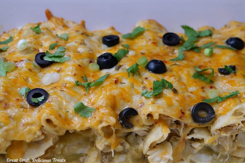 A white baking dish showing the chicken enchiladas with all the cheese, black olives, and shredded chicken.