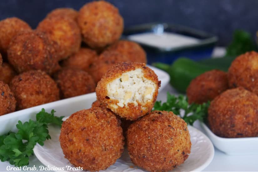 A white plate with four chicken cheese bites on it with a bite taken out of the one on top, with more cheese bites in the background.