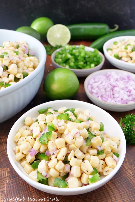 Chipotle Fresh Tomato Salsa is a delicious salsa recipe that is made with diced red onion, jalapenos, white corn, and the perfect blend of seasonings. Two different sized bowls of Chipotle salsa, and three smaller bowls in the background with diced jalapeños, red onion, and half a lime.