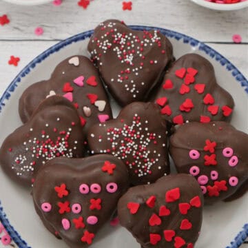 A white surface with a white plate with blue trim with peanut butter hearts covered in chocolate on it with the title overlay at the top.