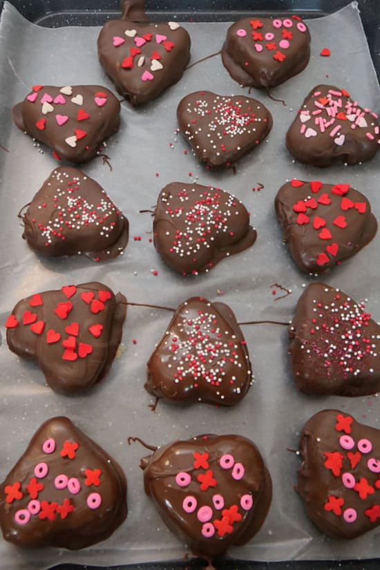 A baking sheet with chocolate covered hearts and Valentine sprinkles on them.