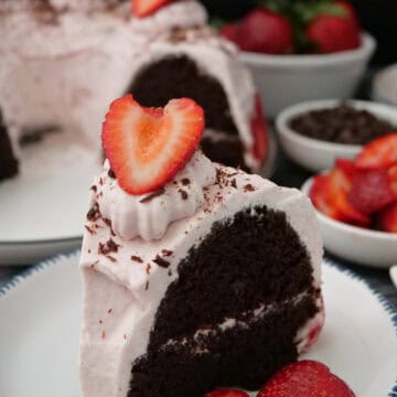 A round white plate with blue trim with a slice of chocolate strawberry cream bundt cake on it with more cake in the background.