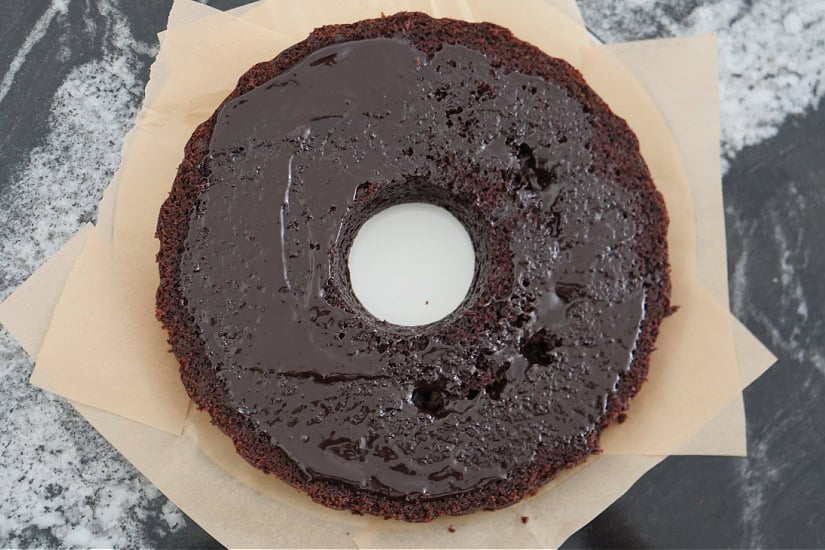 A black counter top with a chocolate bundt cake cut in half lengthwise and a chocolate sauce spread over it.