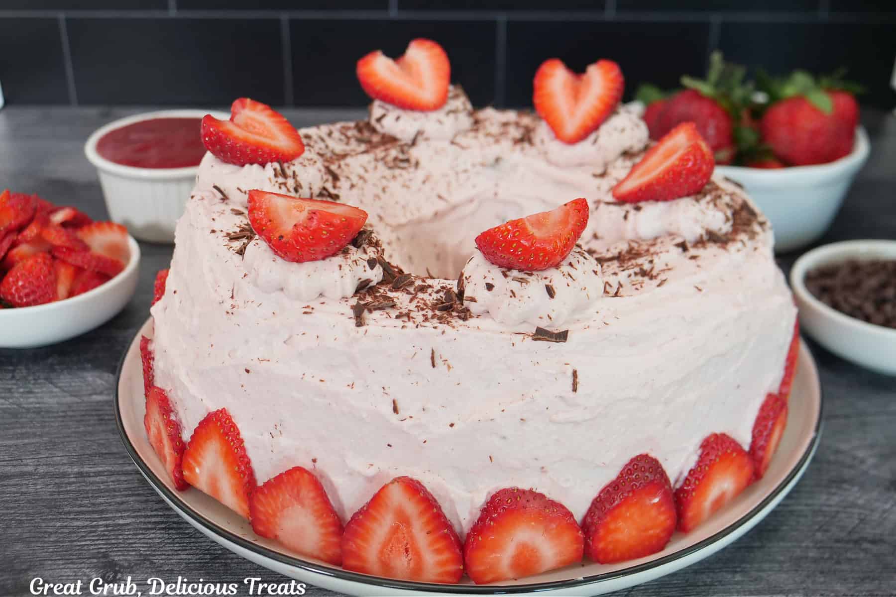 A strawberry whipped cream frosting covering a chocolate bundt cake with thin sliced strawberries around the bottom edge.