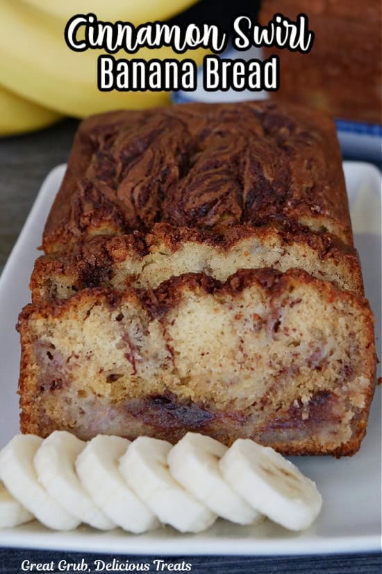 A white plate with a loaf of banana bread on it that has been sliced with sliced bananas on the plate.