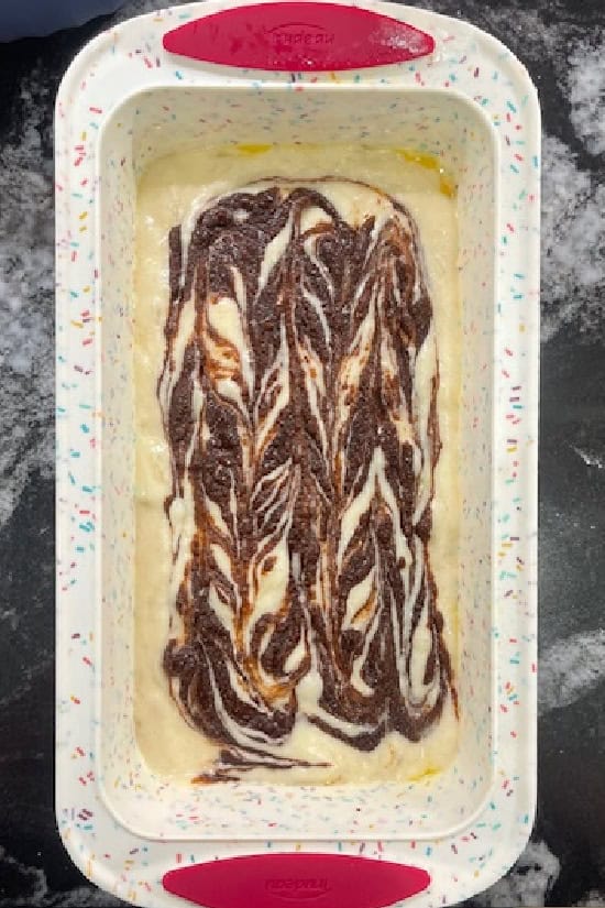 A white loaf pan filled with banana bread with cinnamon swirl added.