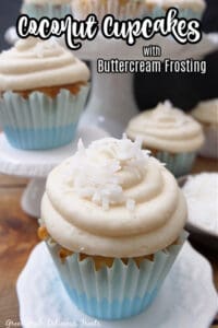 A cupcake in a blue liner with shredded coconut on top, and a cake stand with cupcakes in the background.
