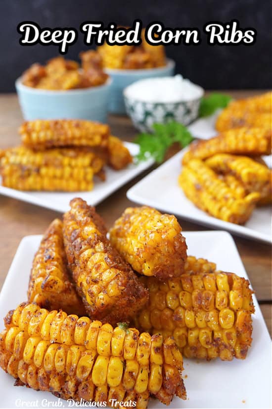 White square plates with fried corn fibs on them with dipping sauce and more corn ribs in the background.