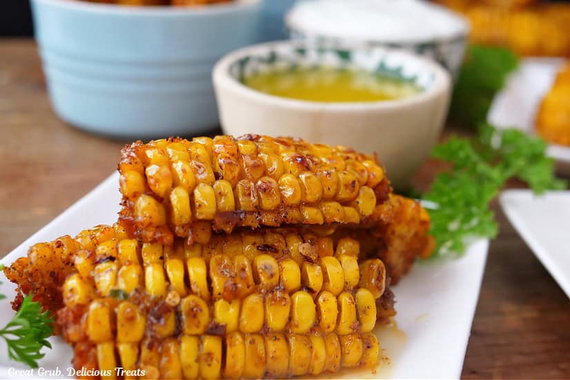 A white square plate with three corn ribs on it with melted butter in the background.