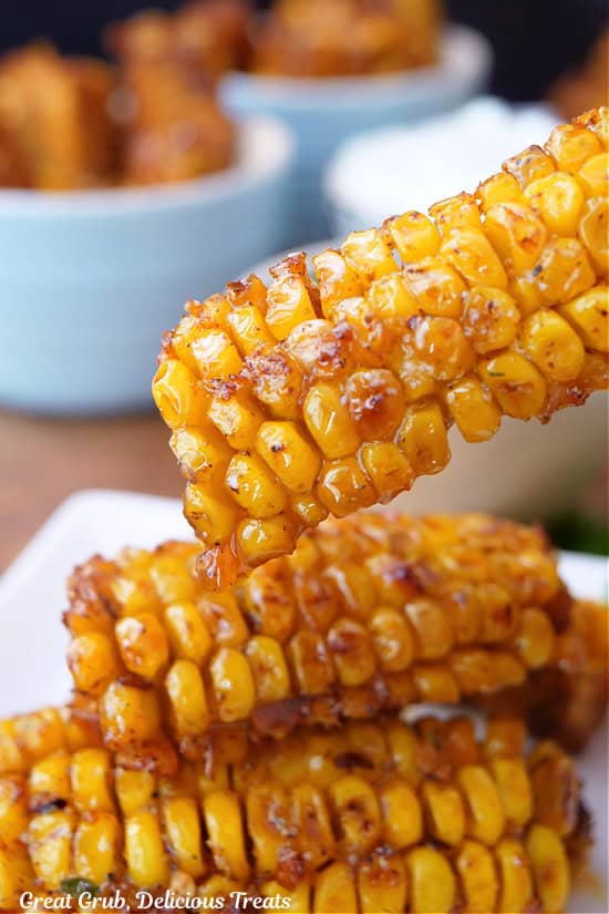 Three deep fried corn ribs with melted butter and seasonings on them.