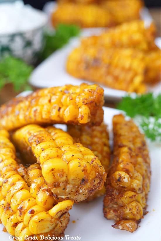 A white square plate with five deep fried corn ribs on it with more ribs in the background.