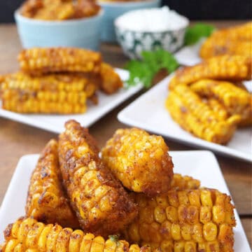 Three white square plates with deep fried corn ribs on them.