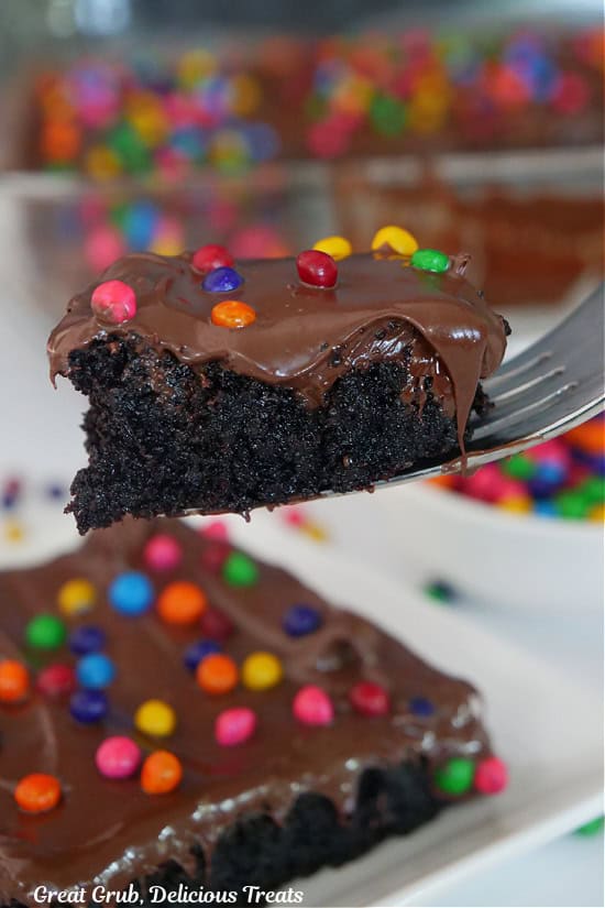 A big bite of chocolate brownie on a fork showing the melting chocolate on top and the rainbow sprinkles.