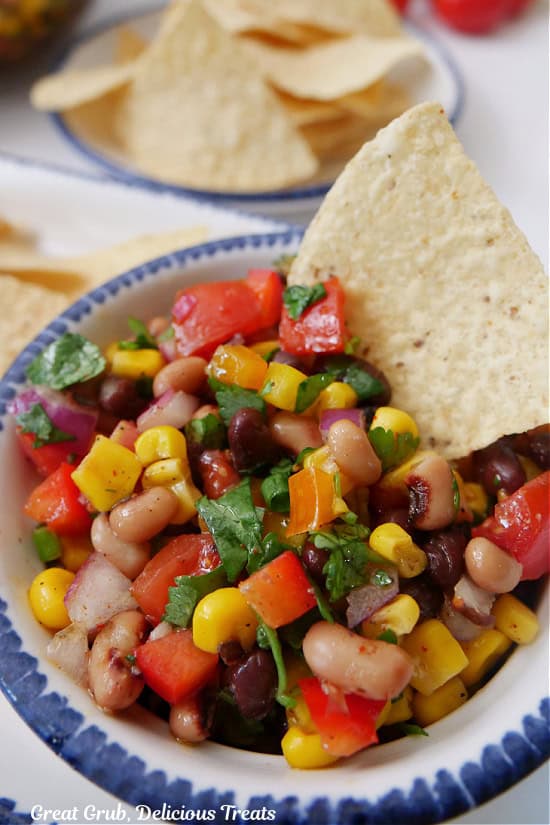 A small white bowl with blue trim filled with cowboy caviar and a tortilla chip in the dip.