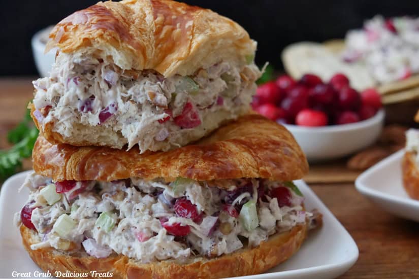 A wood surface with a white square plate with two crescent filled with cranberry chicken salad.