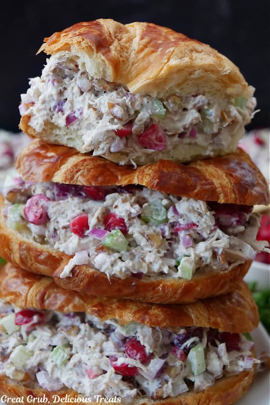 A stack of three cranberry chicken salad crescent sandwiches with a few bites taken out of the top sandwich.