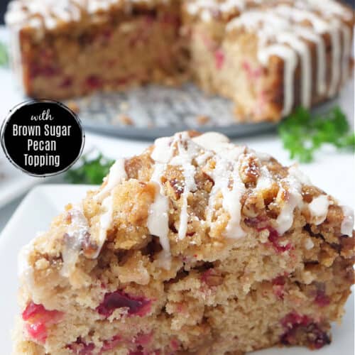 A white plate with a slice of cranberry coffee cake on it with the whole cake in the background.