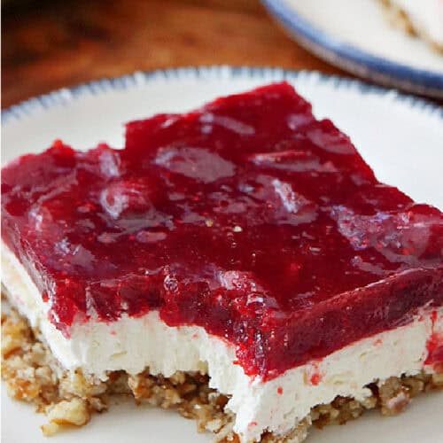 A small round white plate with blue trim with a serving of cranberry Jello salad on it.
