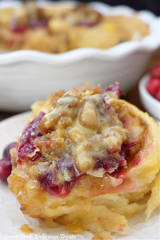 A cranberry orange cinnamon roll on a round plate with more in the background.