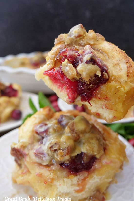 A cinnamon roll, held above another cinnamon roll, with a bite taken out of it.