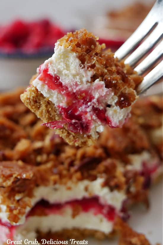 A bite of cranberry orange dessert on a fork held above a serving of the dessert on a round plate.
