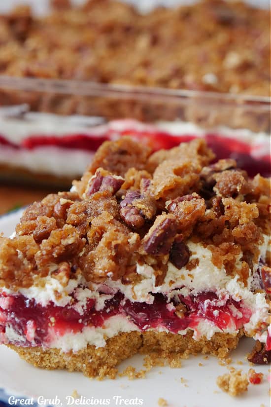 A round plate with a serving of cranberry orange dessert on it with more in a baking dish in the background.