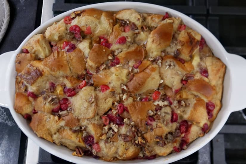 A white oval baking dish with a baked cranberry pecan bread pudding in it.