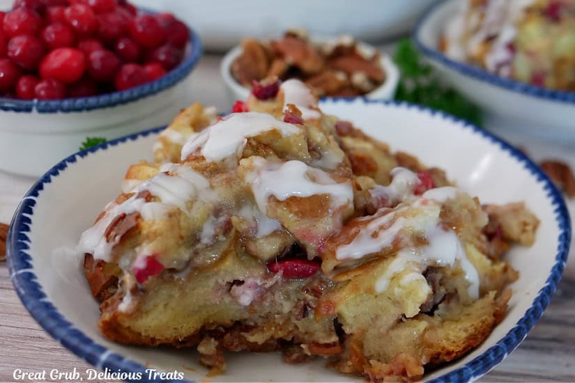 A serving of cranberry pecan bread pudding on a white bowl with blue trim.