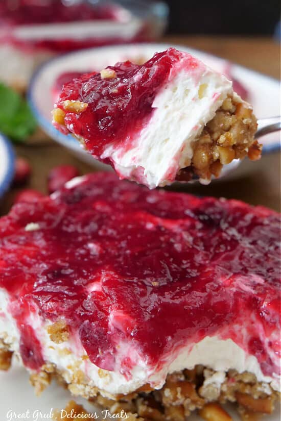 A bite of cranberry pretzel salad on a spoon held above a serving of the dessert.