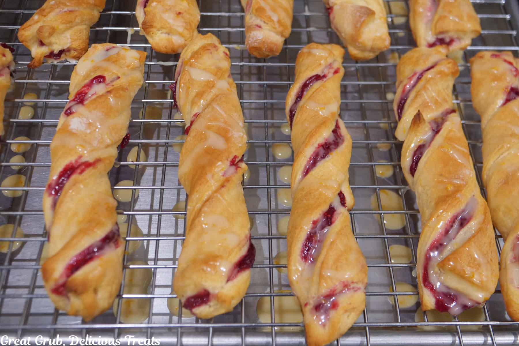 A wire rack with baked cranberry twists on it and covered with orange glaze.