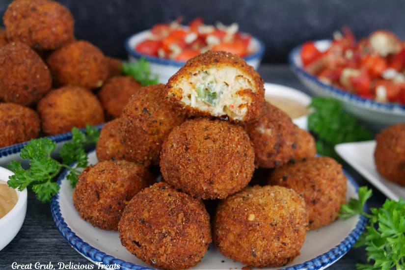 A round white plate with blue time with a stack of crawfish balls on it and the top ball has a bite taken out of it.