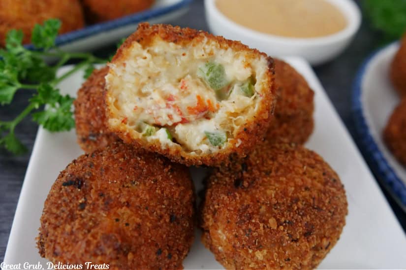Five crawfish balls on a small square white plate with a bite taken out of one of them.