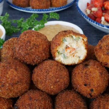A stack of deep fried crawfish balls on a white plate with a bite taken out of the one of top.
