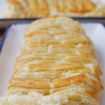 A close up of a cheese danish braid on a white plate with blue trim.