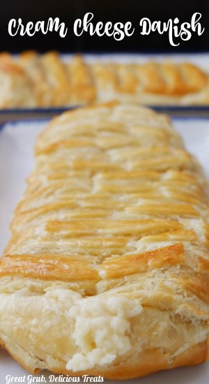 A cheese danish on a bite oblong plate with another danish in the background.