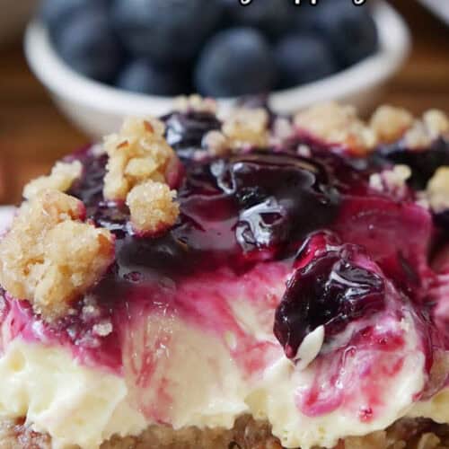 A close up photo of a serving of lemon cream cheese dessert with a small white bowl filled with blueberries in the background.