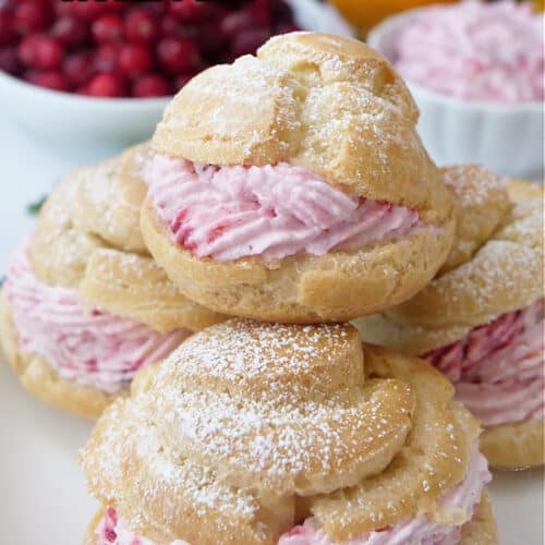 A small round white plate with blue trim with four cream puffs filled with cranberry mousse filling on it.