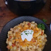 A wood surface with a black bowl filled with a serving of creamy chicken pasta.