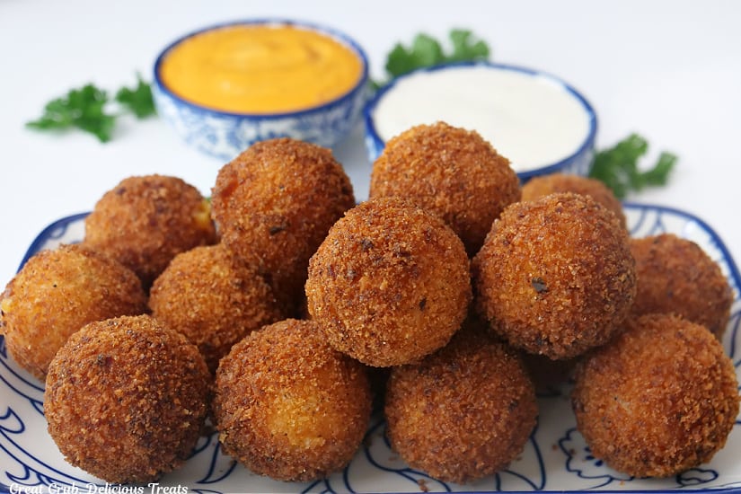 A horizontal photo of a rectangle plate with over a dozen little bite-size cheese bites on it.