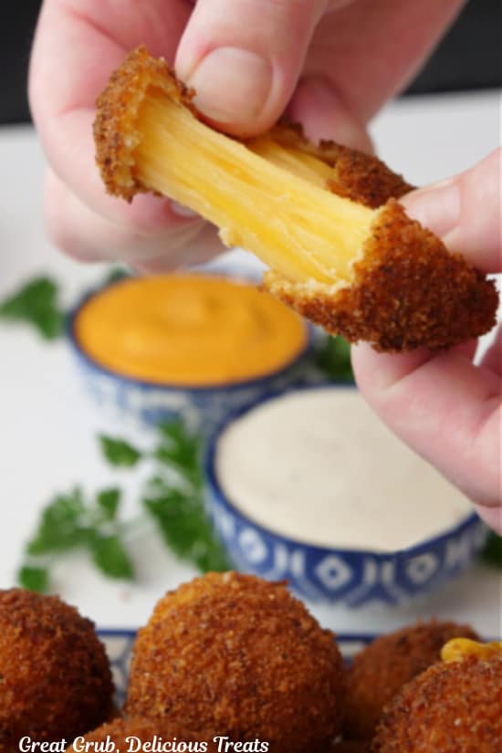 A cheese bite being broken in half showing the gooey cheese inside.