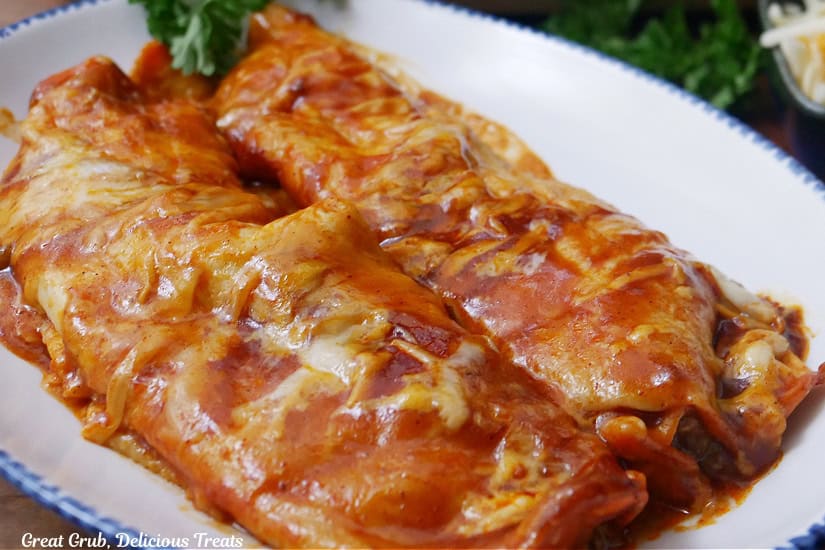 A white oval plate with blue trim with two beef enchiladas on it.