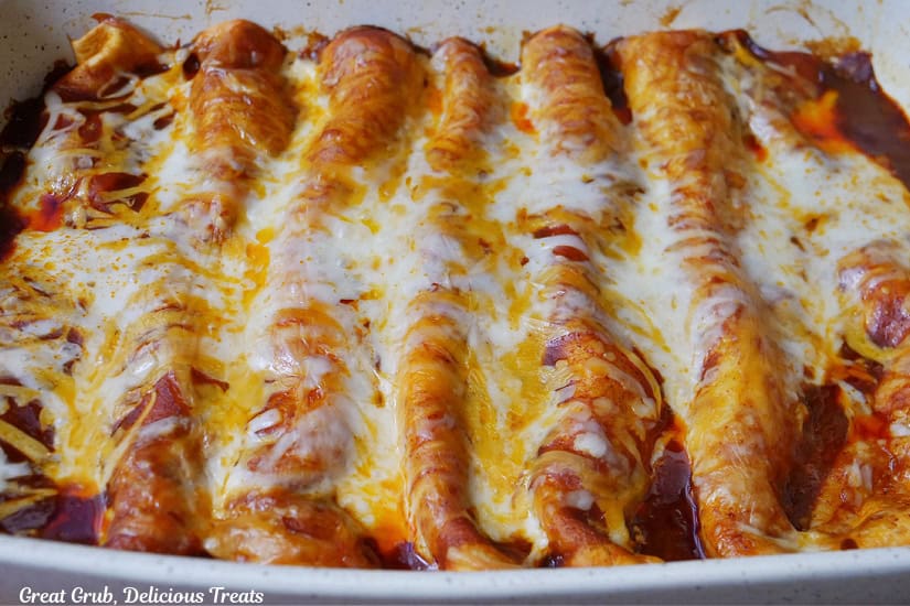A white baking dish filled with 7 beef enchiladas after being baked and removed from the oven