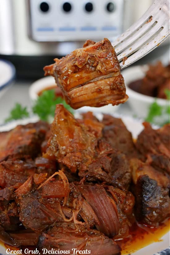 A bite of beef ribs on a fork held above a plate of boneless ribs.